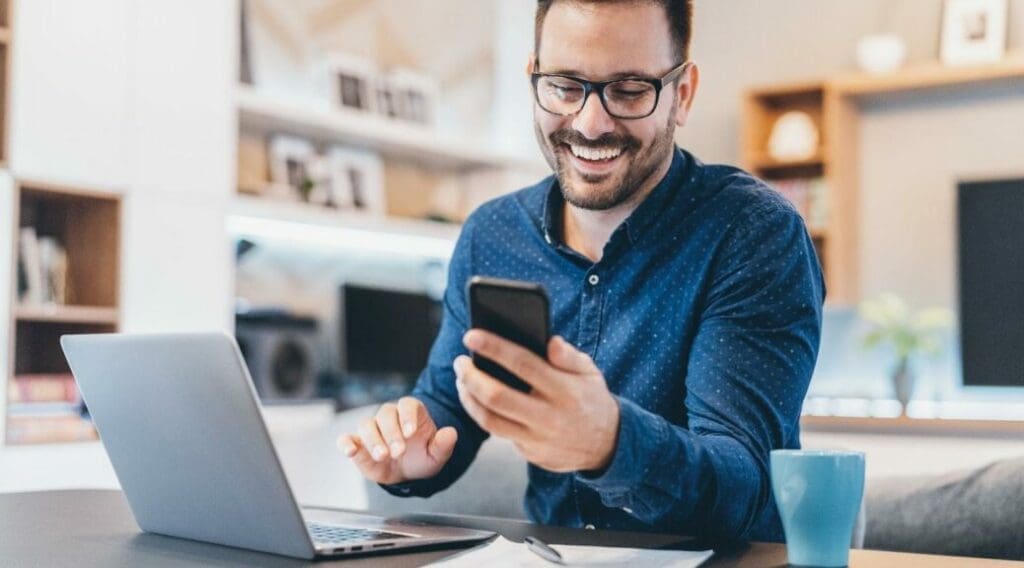Man sitting in front of laptop smiling holding phone