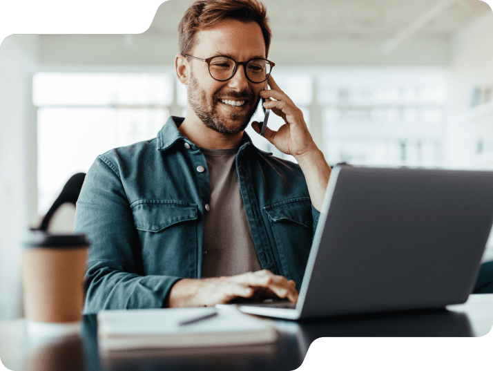 Man smiling holding phone while on laptop