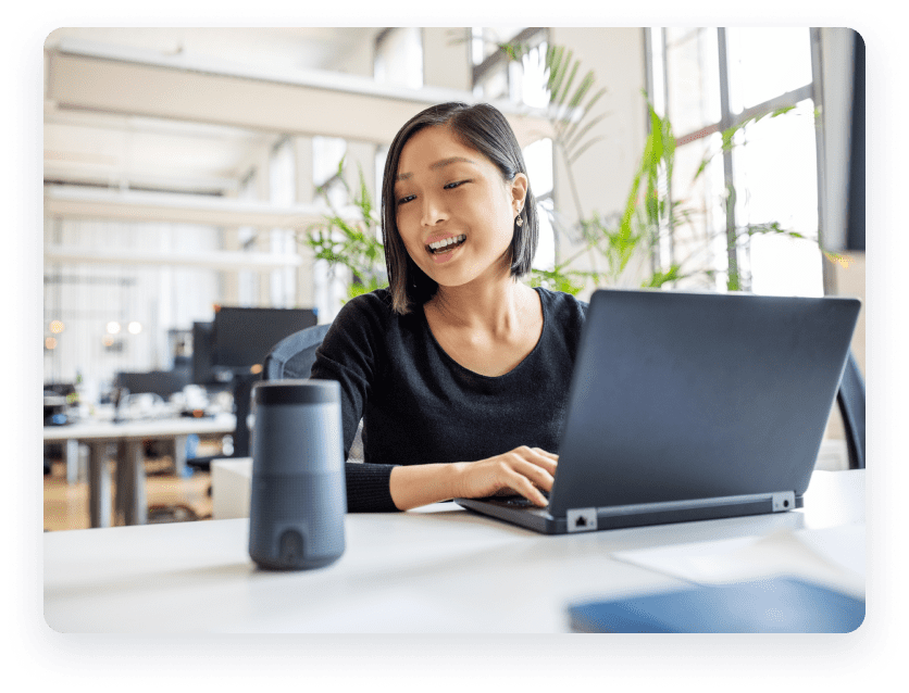 Woman on laptop next to a wireless speaker.