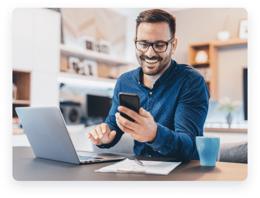 Man smiling on phone and laptop.