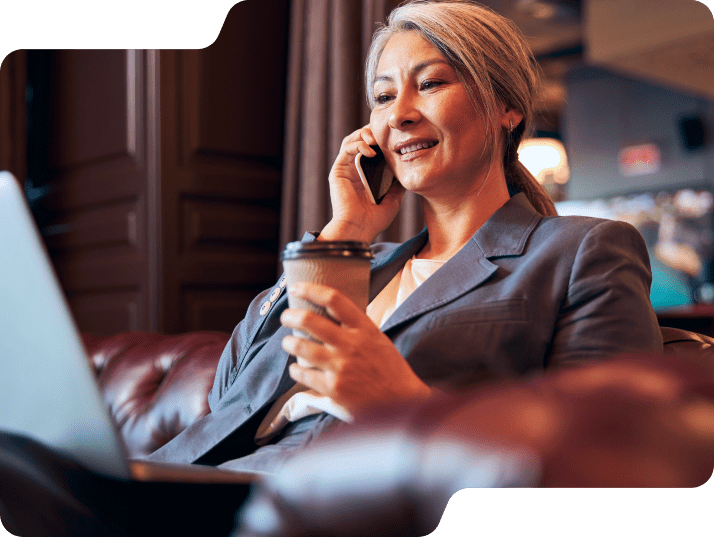 Woman holding coffee on the phone while looking at laptop