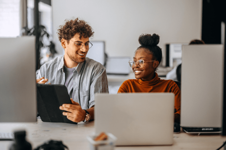 Two business professionals having a discussion in a shared workspace, using digital devices. Represents teamwork and effective business communication solutions.