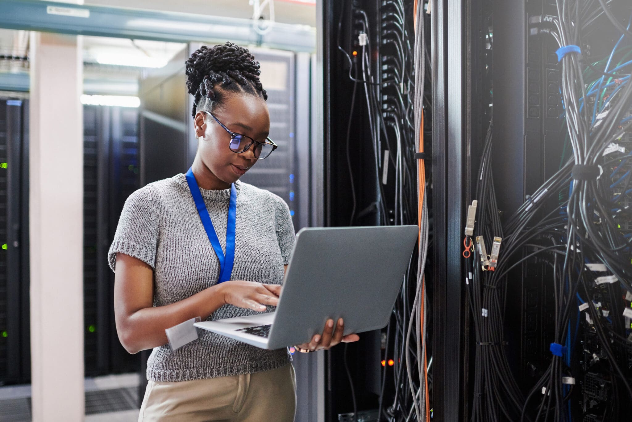 Female IT technician inspecting server cables and monitoring systems in a data centre to prevent communication downtime