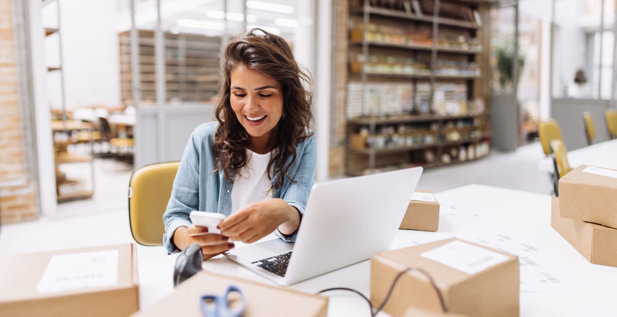 Female business owner using a VoIP phone while working on a laptop in a Canadian shipping centre.