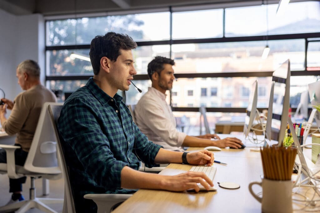 Customer service agents using VoIP headsets in a professional office environment with desktop monitors.