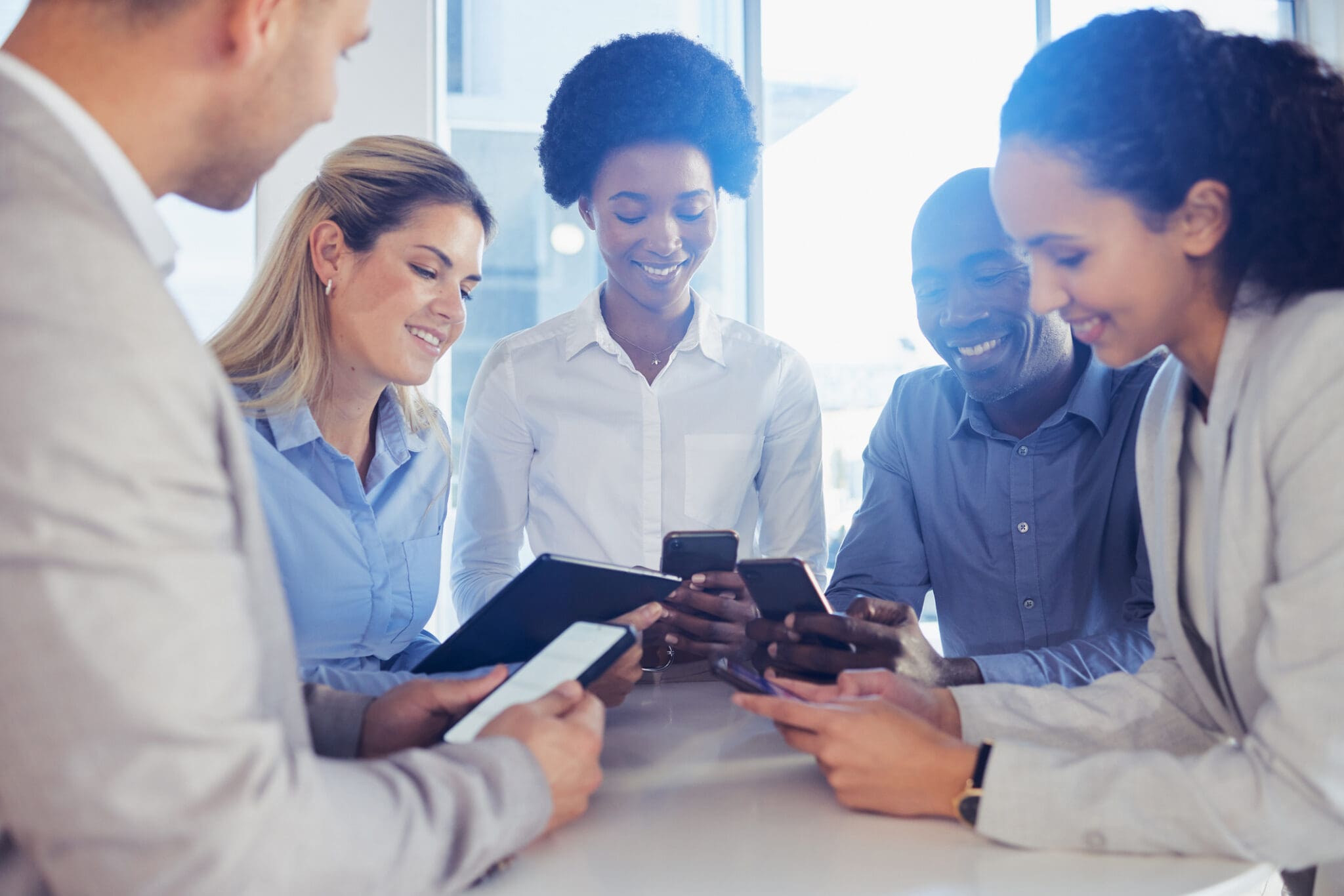 Diverse business team engaged in a discussion while using smartphones and tablets, showcasing real-time communication through VoIP and SMS.