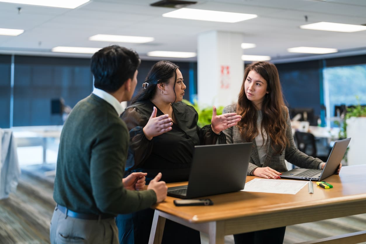 Three professionals in a modern office setting discuss PBX and voIP phone systems with their laptops on the desk, symbolizing scalable communication and support for business growth.