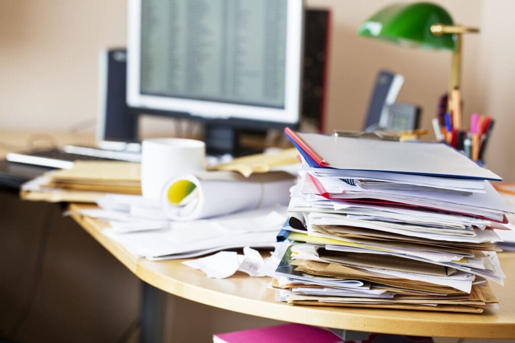 A cluttered office desk with stacks of paper highlights the benefits of electronic faxing as a digital tool to reduce waste.