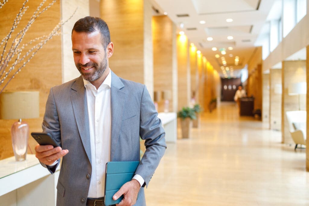  Hotel manager in a bright hotel lobby checking messages on a smartphone that is connected to a business phone system.