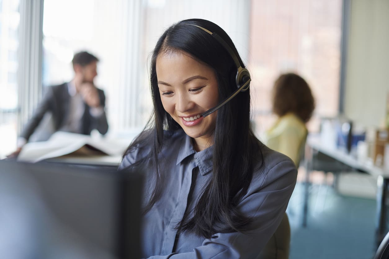 Customer service agent using a headset to answer calls through a PBX system in a professional office environment.